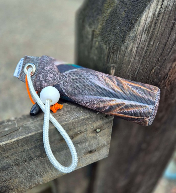 Dog & Field Original Clone 100g teal dummy resting on fence in field - realistic HD teal feather print canvas training dummy for gundog marking and retrieve work